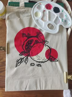 a tote bag sitting on top of a wooden table next to paints and brushes