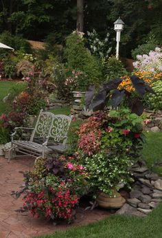 a garden filled with lots of flowers and plants next to a stone walkway in the middle of a lush green field