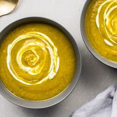 two bowls filled with soup sitting on top of a white table next to silver spoons