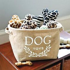 stuffed giraffes sit in a dog toy basket on a table next to a bone