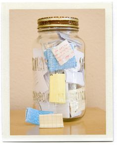 a glass jar filled with lots of different types of paper and magnets on top of a wooden table