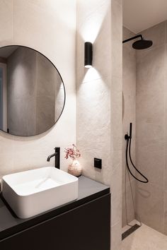 a white sink sitting under a bathroom mirror next to a walk in shower with a black faucet