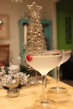 two martini glasses sitting on top of a counter next to a christmas tree in the background