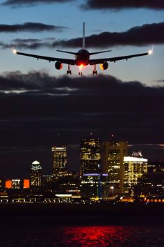 an airplane is flying over the city skyline at night with its landing lights lit up