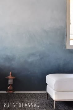 a white couch sitting next to a window on top of a carpeted floor in front of a blue wall