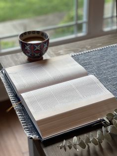 an open book sitting on top of a wooden table next to a cup of coffee