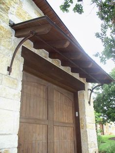 an open wooden door on the side of a stone building with a metal awning over it