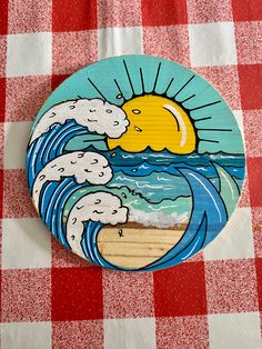 a wooden plate with an image of the sun and waves on it sitting on a checkered tablecloth