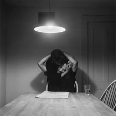 a black and white photo of a woman sitting at a table with her head in her hands