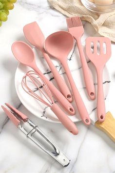 pink kitchen utensils are sitting on a marble countertop next to a bowl with grapes