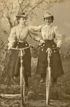 an old photo of two women on bicycles posing for the camera with their arms around each other