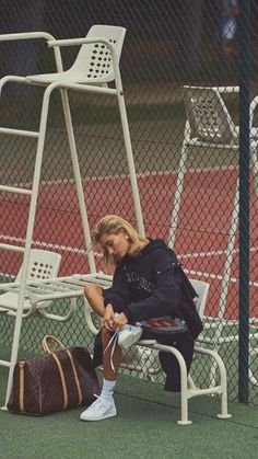 a woman sitting on a bench next to a tennis racquet and luggage bag