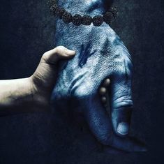 two hands holding each other in the middle of a dark background with blue paint on them