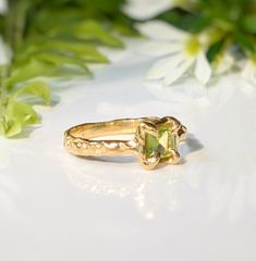 Show your love with this exquisite Peridot ring. Handcrafted in wax and cast in Solid 14k Gold, this stunning green crystal ring features an organic textured band, ensuring its uniqueness. Adorned with a mesmerizing princess-cut Peridot, also the August birthstone, it embodies more than an engagement ring - it symbolizes timeless love and individualityT H E ∙ S M A L L ∙ D E T A I L S• Princess-cut Peridot (5 x 5mm)• Solid 14k Gold textured bandM A T E R I A L ∙ O P T I O N S• Sterling Silver• S Peridot And Diamond Engagement Rings, Organic Gold Engagement Ring, Peridot Solitaire Jewelry For May Birthstone, Wedding Jewelry In Yellow Gold With Tsavorite, Yellow Gold Tsavorite Wedding Jewelry, Elegant Green Jewelry In Recycled Gold, Fine Green Citrine Jewelry, Heirloom Green Promise Ring, Emerald Cut Peridot Ring For May Birthstone