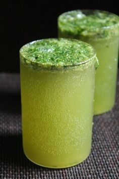 two glasses filled with green liquid on top of a table