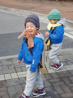 two young boys walking down the street with their backpacks on and one holding his hand up to his mouth