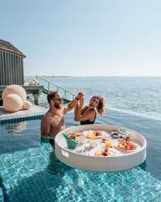 a man and woman standing next to a swimming pool with food on the trays