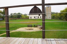 an old barn sits in the distance behind a fenced in area with picnic tables and benches