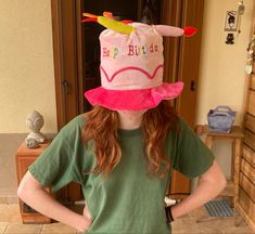 a girl wearing a pink birthday hat standing in front of a door with her hands on her hips