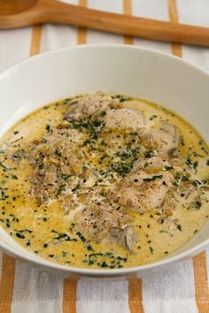 a white bowl filled with soup sitting on top of a striped table cloth next to a wooden spoon