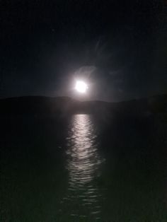 the full moon shines brightly in the dark night sky over the water's surface