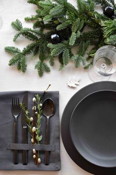 a place setting with black plates, silverware and greenery on the napkins