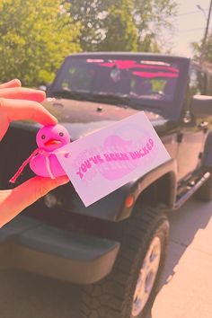 a hand holding a pink rubber duck next to a jeep