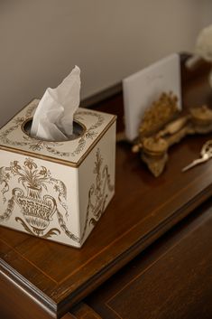 a tissue box sitting on top of a wooden desk next to a gold spoon and napkin dispenser