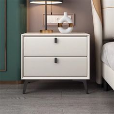 a night stand with two drawers and a lamp on it next to a white bed