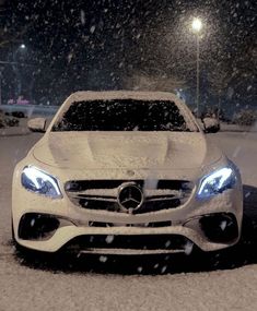 a white car is parked in the snow at night with its hood up and lights on