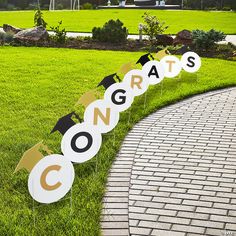 graduation decorations are lined up on the grass in front of a brick path and grassy area