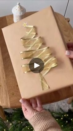 a person holding a wrapped present in front of a christmas tree with gold foil on it