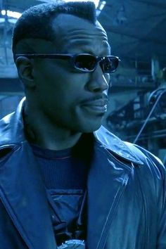 a man with sunglasses and a leather jacket in a warehouse area looking off into the distance