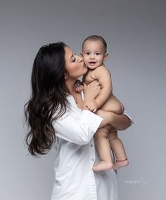 a woman is holding a baby and kissing her cheek while she holds it up in the air