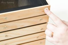 a person's hand pointing at an oven on top of a wooden cabinet with drawers