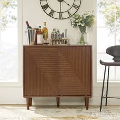 a wooden cabinet with bottles and glasses on it in front of a large wall clock