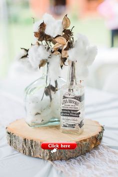 a glass bottle filled with cotton sitting on top of a wooden slice next to flowers