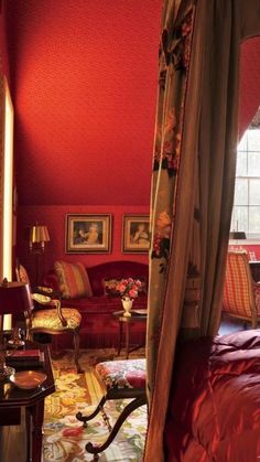 a bedroom with red walls and furniture in the corner, along with paintings on the wall