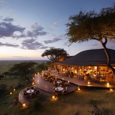 an outdoor dining area with candles lit on the tables and in front of trees at dusk