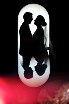 the silhouette of a bride and groom in front of an illuminated vase with their shadow