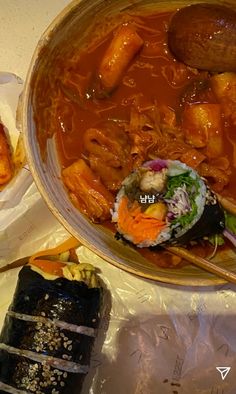 a bowl filled with meat and vegetables on top of a table next to sushi rolls