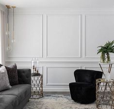 a living room with two black chairs and a gray couch in front of a white wall