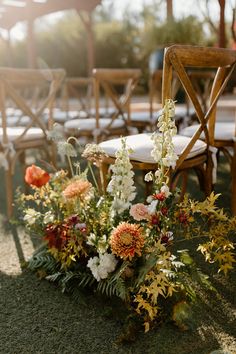 an arrangement of flowers and greenery sits on the ground in front of rows of chairs