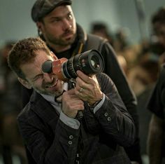 a man holding a camera up to his face while another man looks through the lens