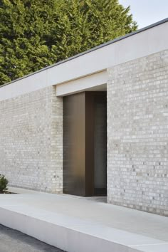 an open door on the side of a white brick building with trees in the background