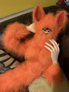 an orange stuffed animal with blue eyes on it's head sitting on a couch