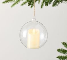 a candle in a glass ornament hanging from a christmas tree