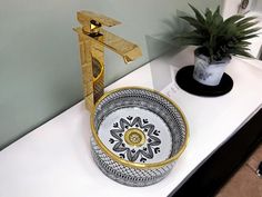 a white counter top with a gold faucet and black and white bowl on it