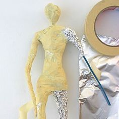 a yellow plastic mannequin next to a roll of tin foil and a tape measure