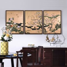 three paintings hang on the wall above a dining room table with chairs and a vase filled with flowers